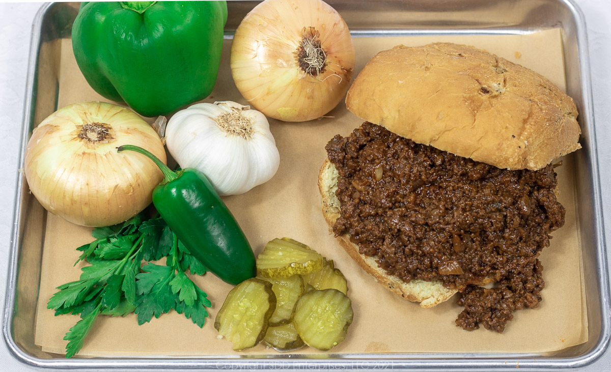 Sloppy Joes on a bun with onions, peppers, garlic, pickles and parsley garnish