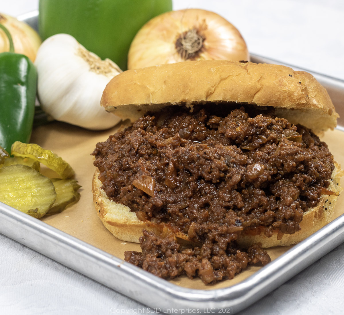 sloppy joe sandwich on a platter with onions, peppers, garlic and pickles as garnish