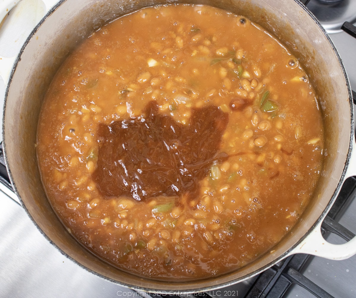 fixings added to canned beans cooking in a Dutch oven.