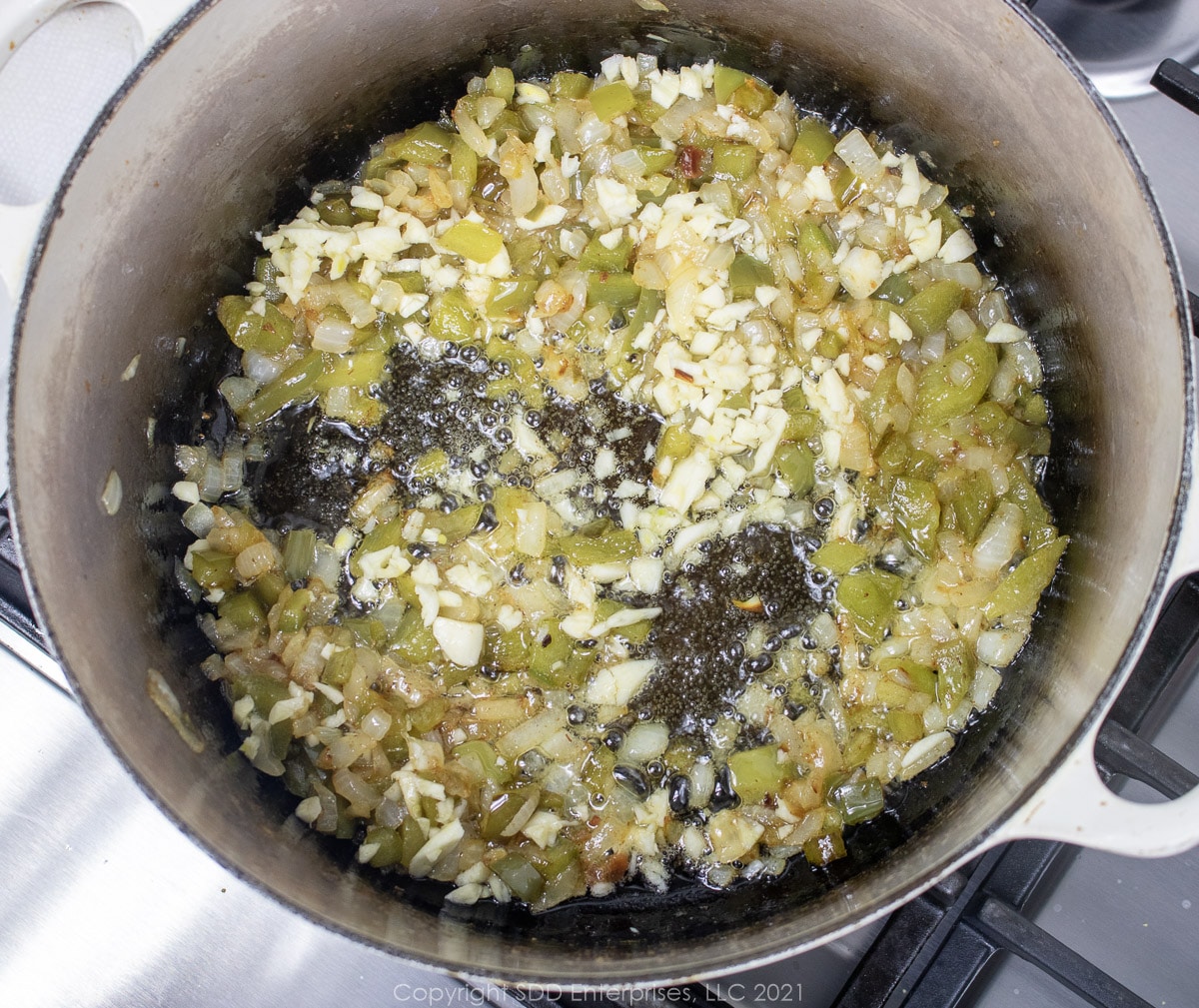 garlic with yellow onions and bell peppers frying in a Dutch oven