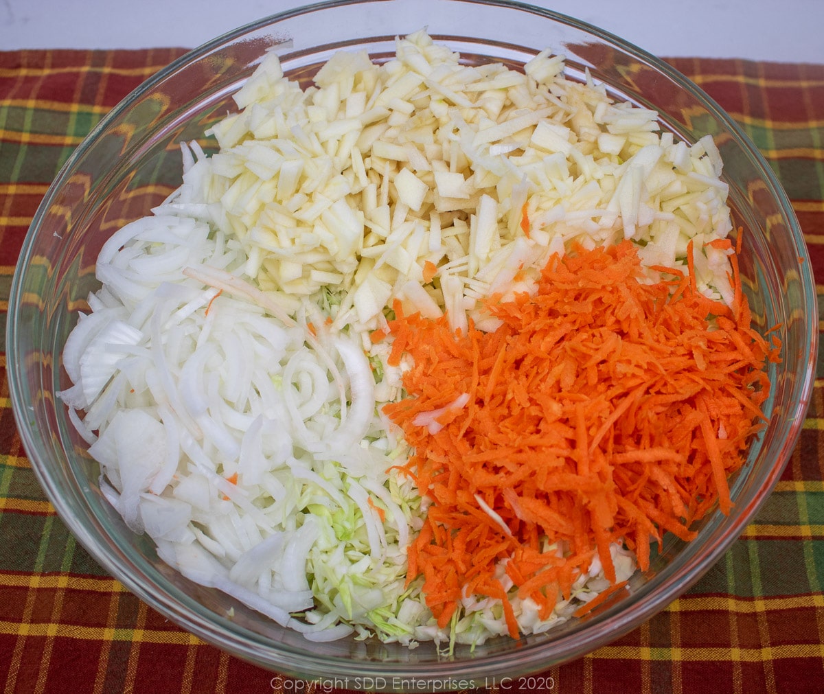 shredded cabbage, onions, carrots and apples in a glass bowl