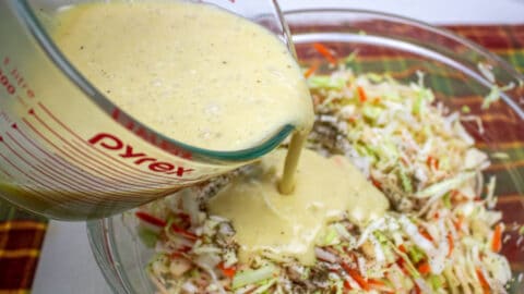 dressing being poured onto chopped cabbage, onions, apples and carrots