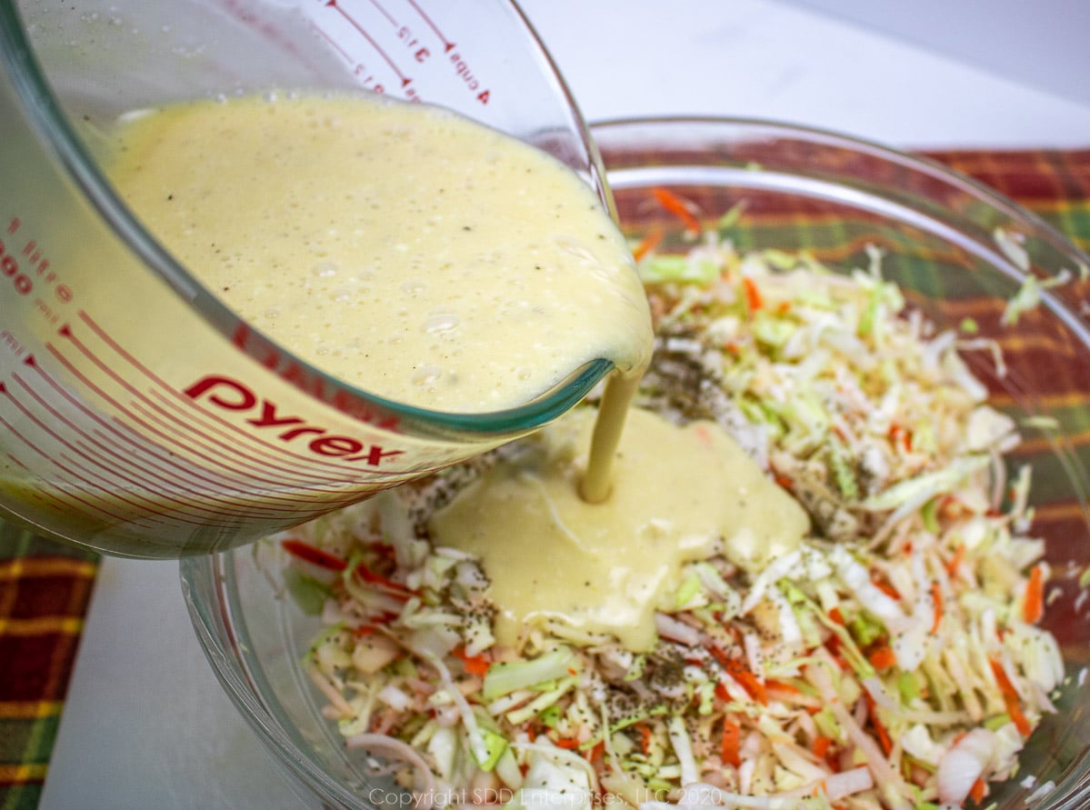 dressing being poured onto chopped cabbage, onions, apples and carrots