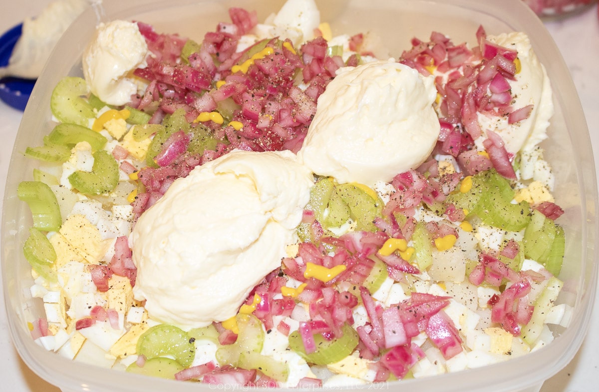 mayonnaise and yellow mustard added to boiled potatoes and eggs in a mixing bowl