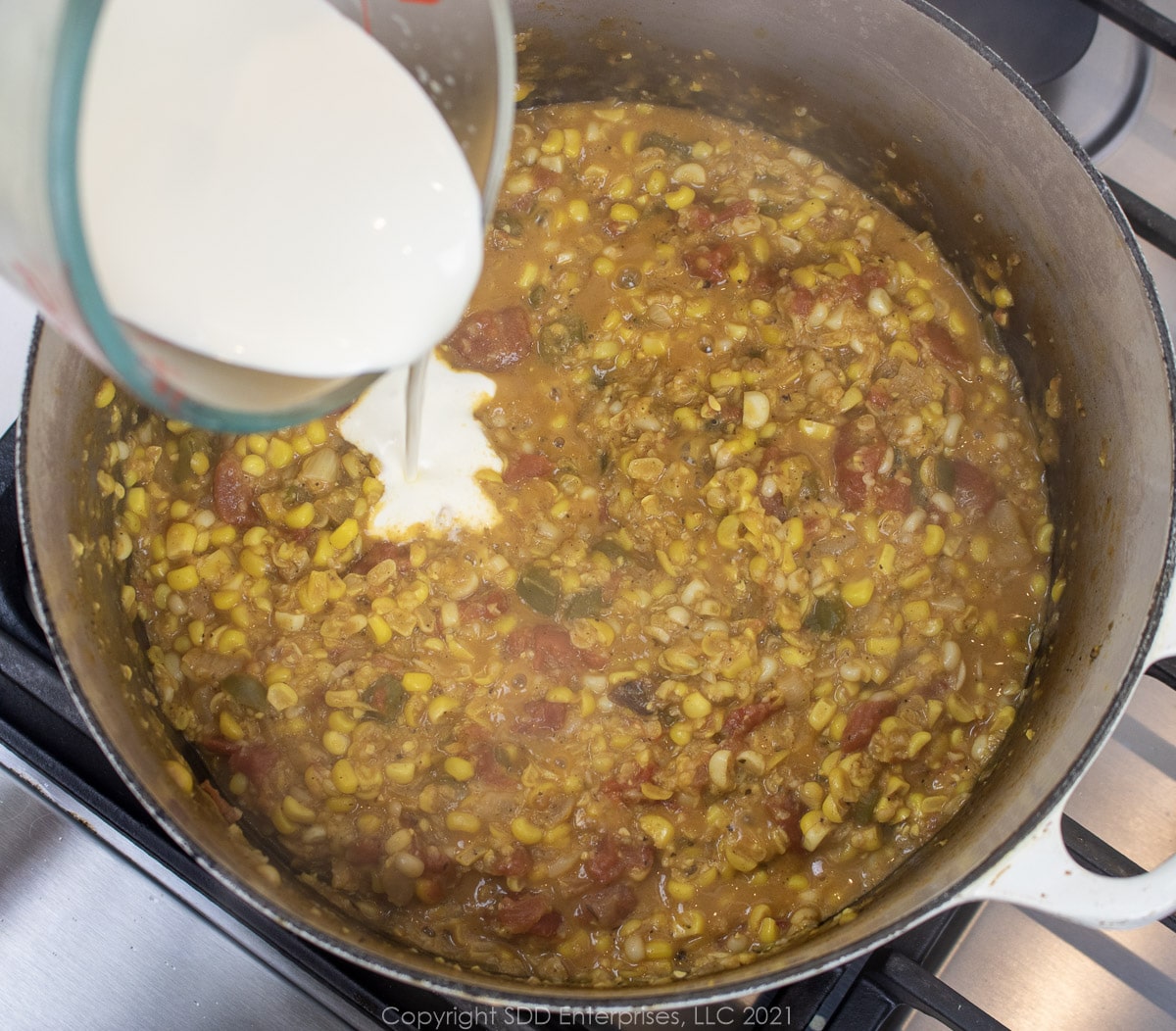 heavy cream being poured into Dutch oven with corn maque choux