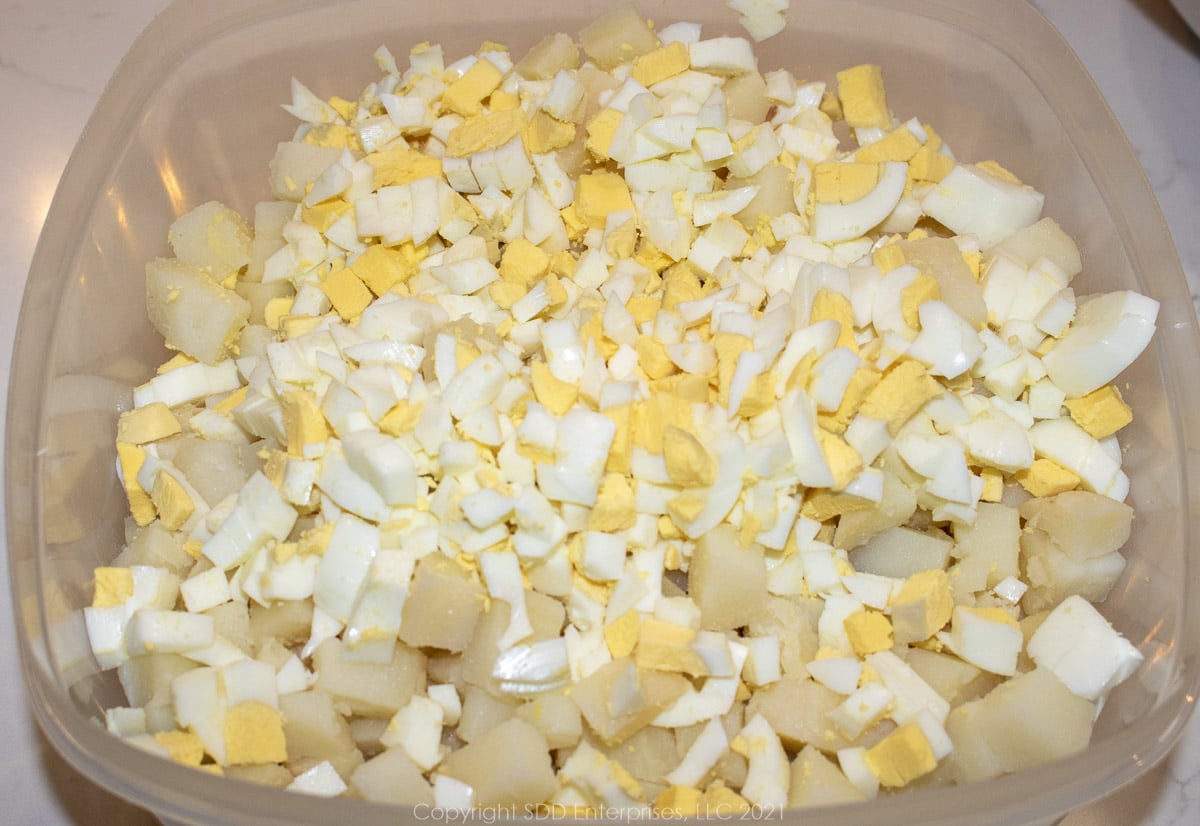 chopped eggs on top of chopped potatoes in a mixing bowl