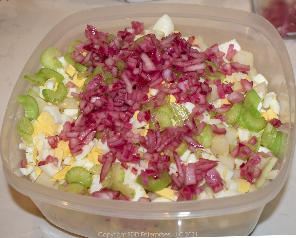 marinated onions and chopped celery added to boiled eggs and potatoes in a mixing bowl