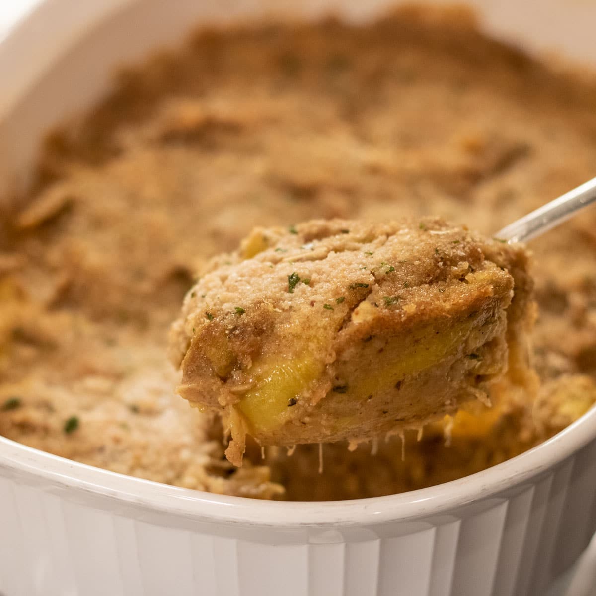 yellow squash casserole on a spoon over casserole dish