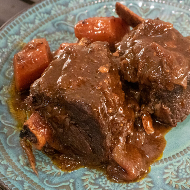 braised beef short ribs with gravy and carrots on a blue-green plate