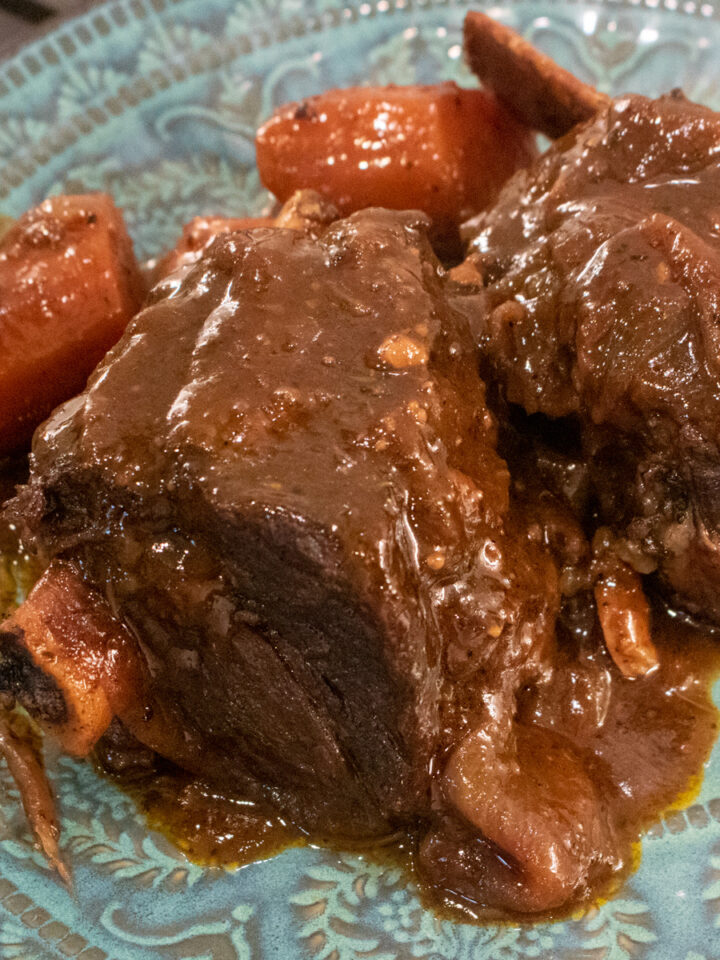 braised beef short ribs with gravy and carrots on a blue-green plate