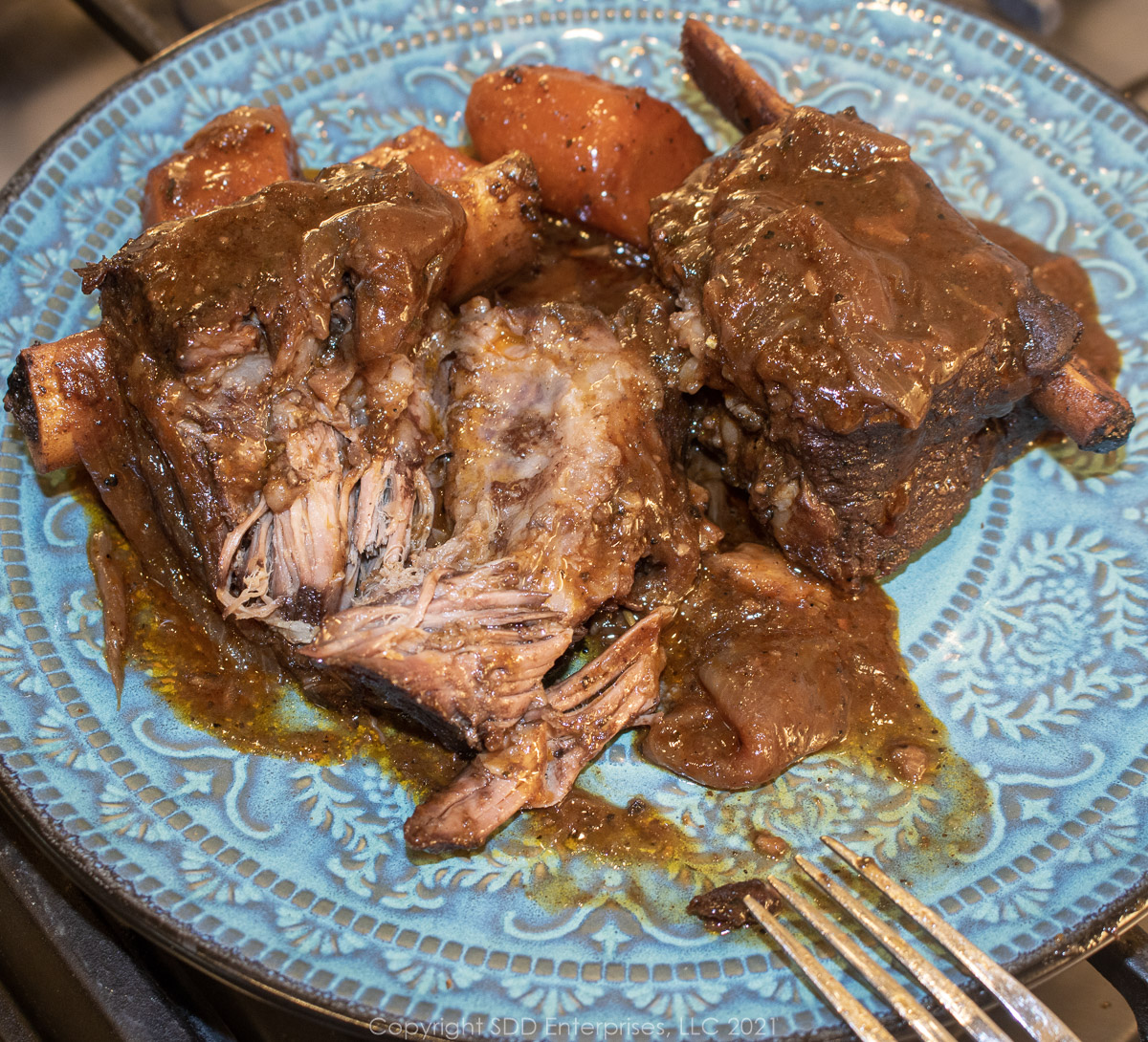 braised beef short ribs with gravy and carrots on a blue-green plate