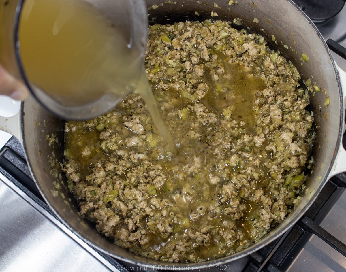 adding stock to simmering pork and vegetables in a Dutch oven