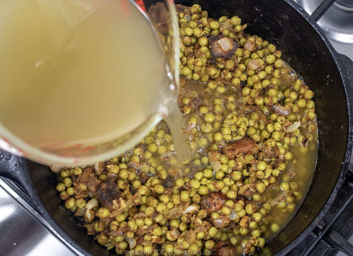 stock being poured into seasoned peas in a Dutch oven