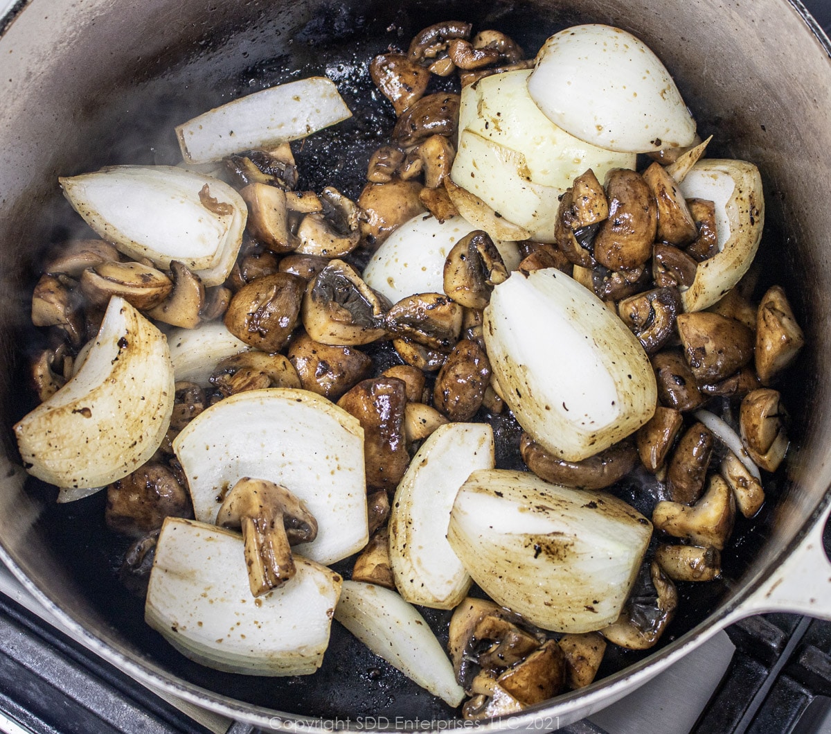 onions added to mushrooms in a Dutch oven