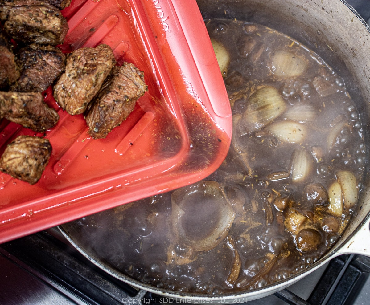 adding beef and juice to a Dutch oven