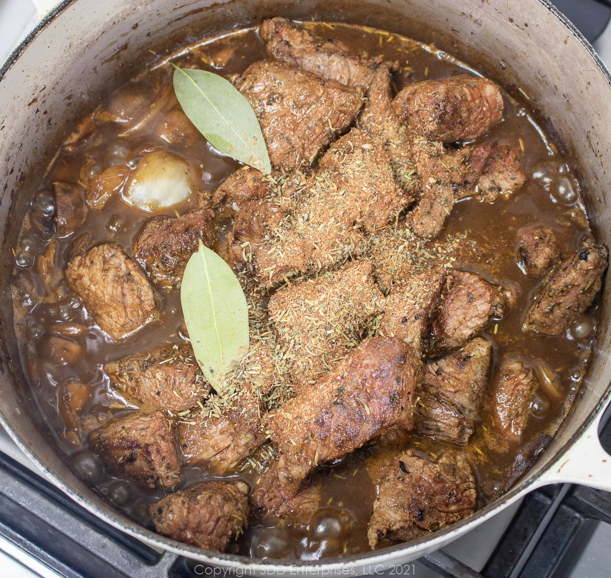 herb and spices added to beef and stock in a Dutch oven