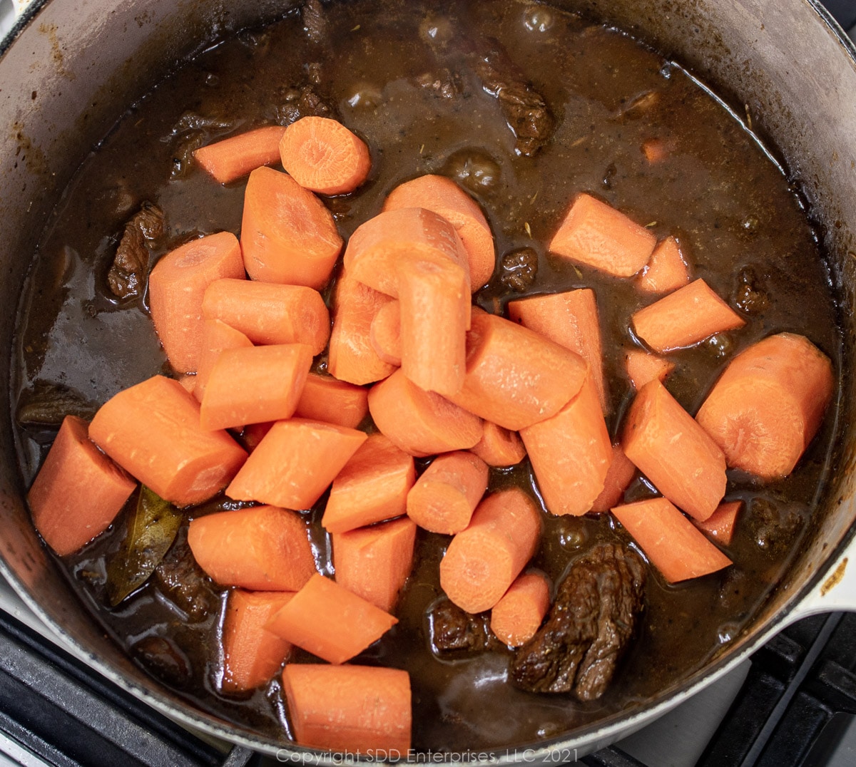 carrots are added to beef and stock in a Dutch oven