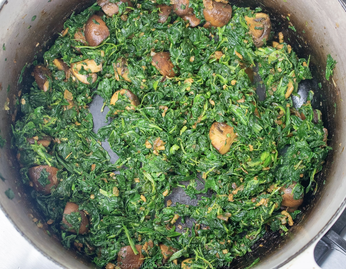 drained spinach added to mushrooms and shallots in a cast iron skillet