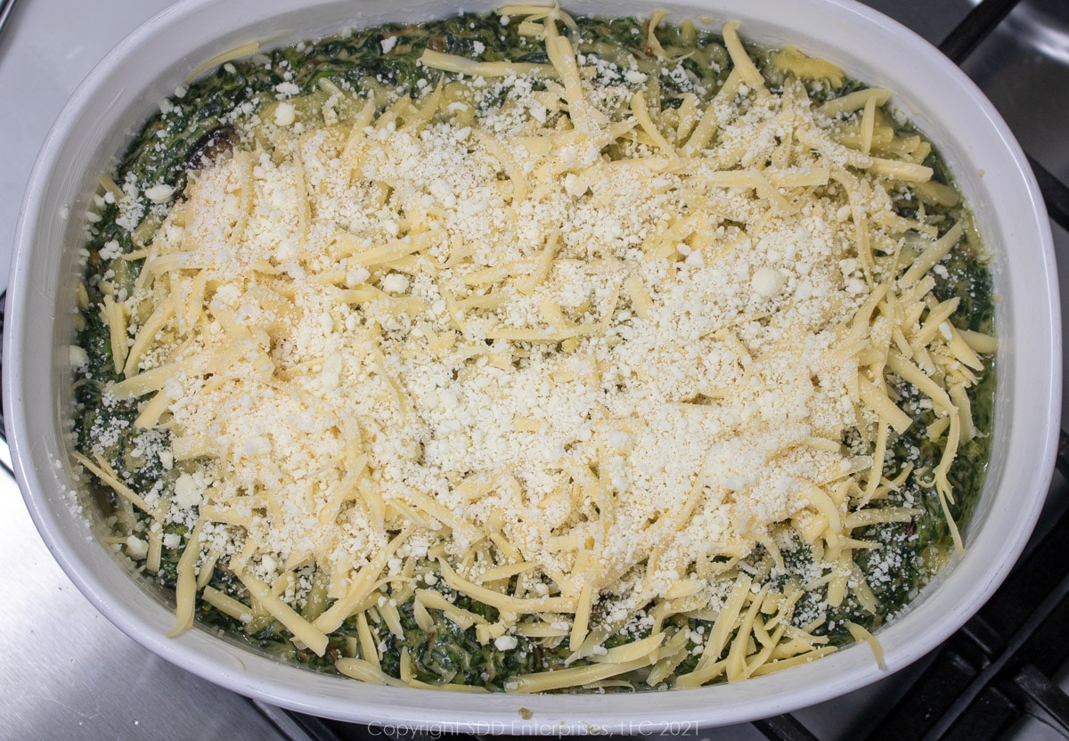 creamy spinach topped with cheese in a baking dish ready for the oven