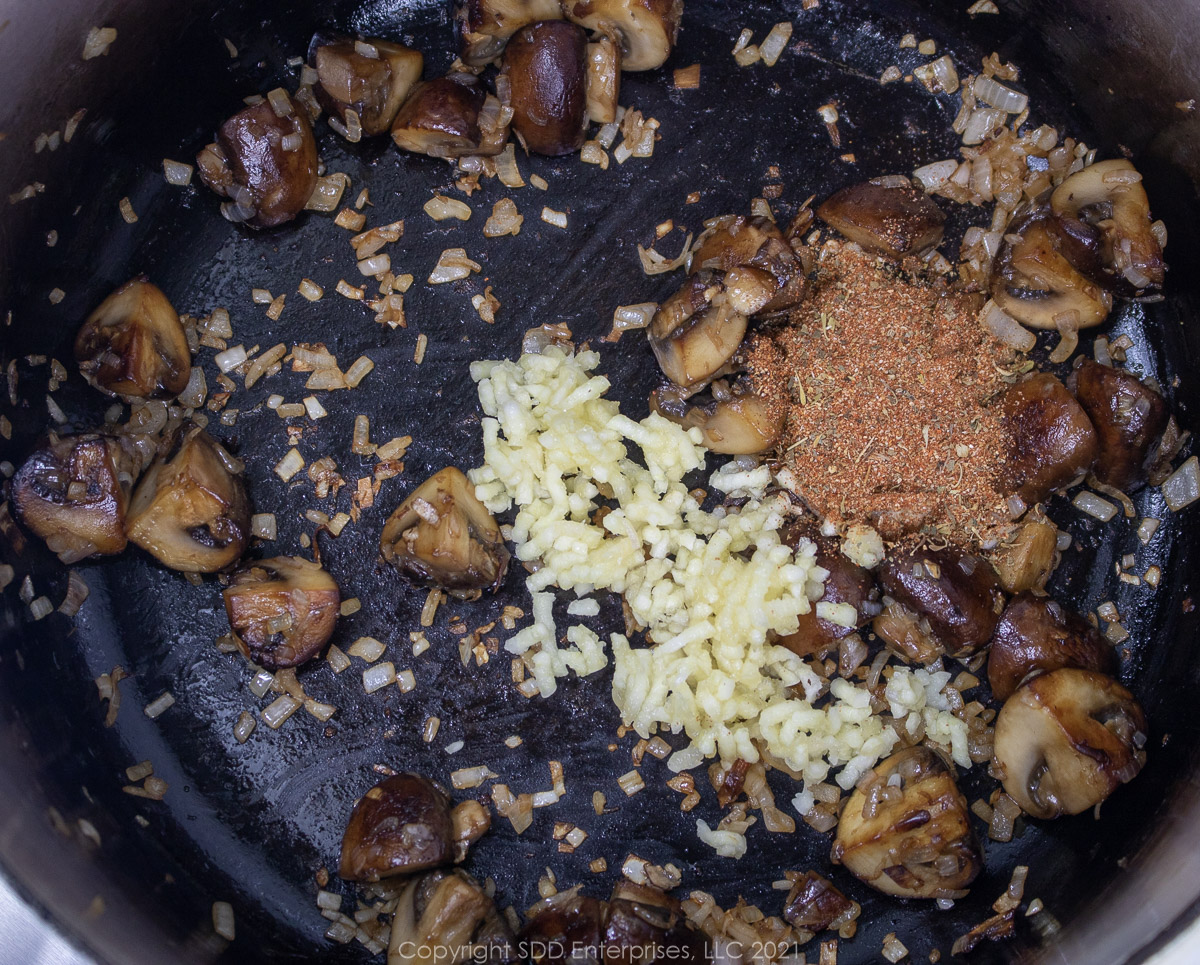 spices added to shallots and mushrooms in a cast iron skillet