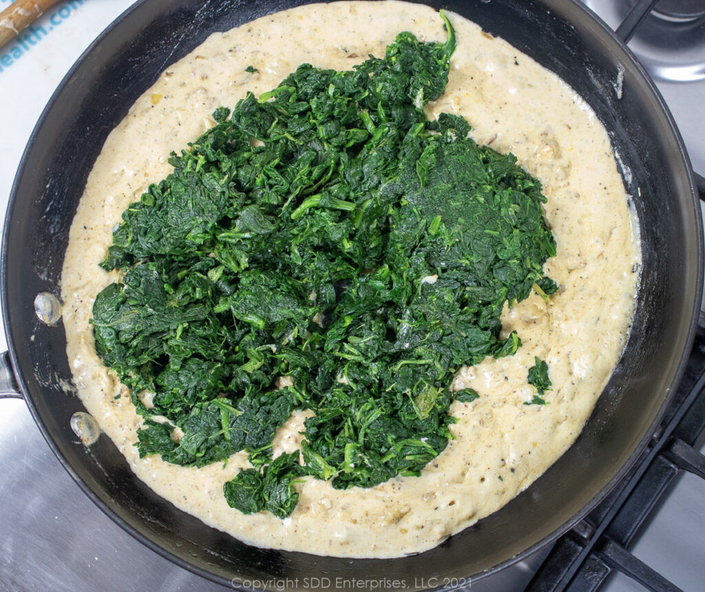 Spinach added to cream sauce in a saute pan.