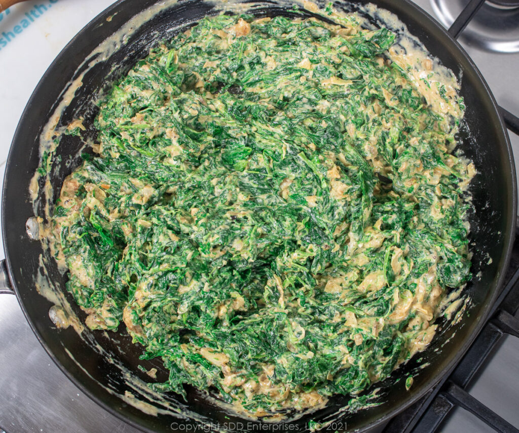 Spinach blended into cream sauce in a saute pan.