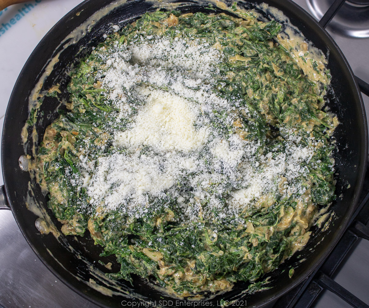 romano cheese added to creamed spinach in a sauté pan
