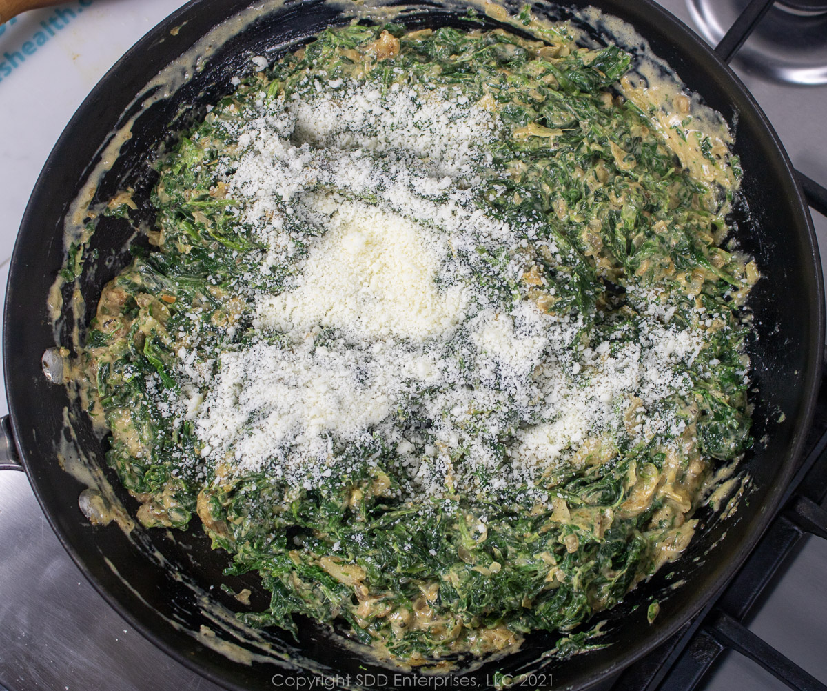 romano cheese added to creamed spinach in a sauté pan