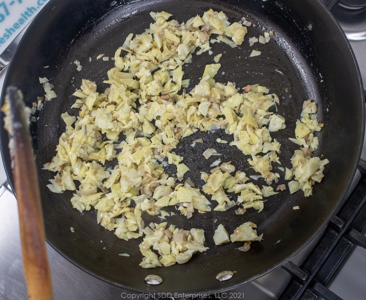 chopped artichoke hearts with shallots in a sauté pan