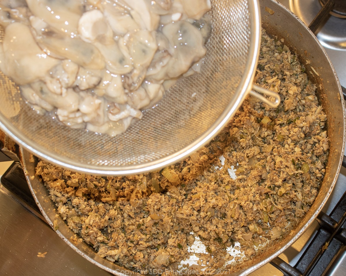 fresh raw oysters being added to poultry meat and vegetables in a stock pot