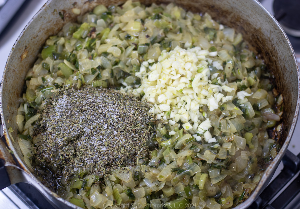 garlic and herbs and spices added to onions and celery in a frying pan