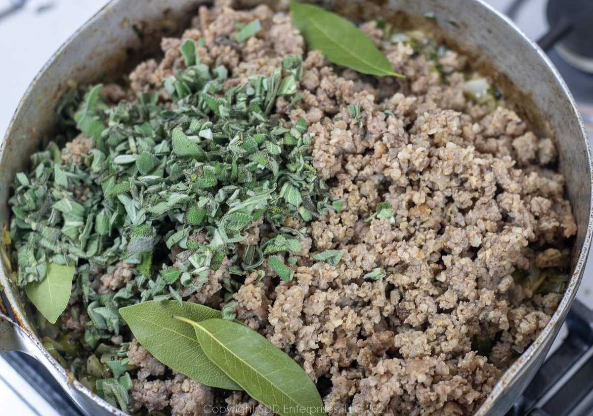 browned pork sausage with fresh sage and bay leaves added to onions in a frying pan