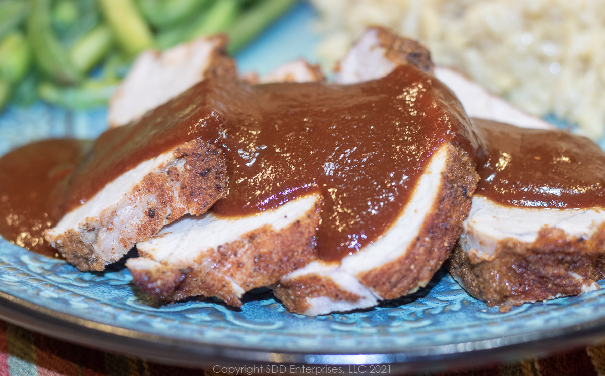 cranberry bbq sauce poured over pork tenderloin on a green dinner plate