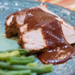 cranberry bbq sauce poured over port tenderloin with a side of green beans on a green dinner plate