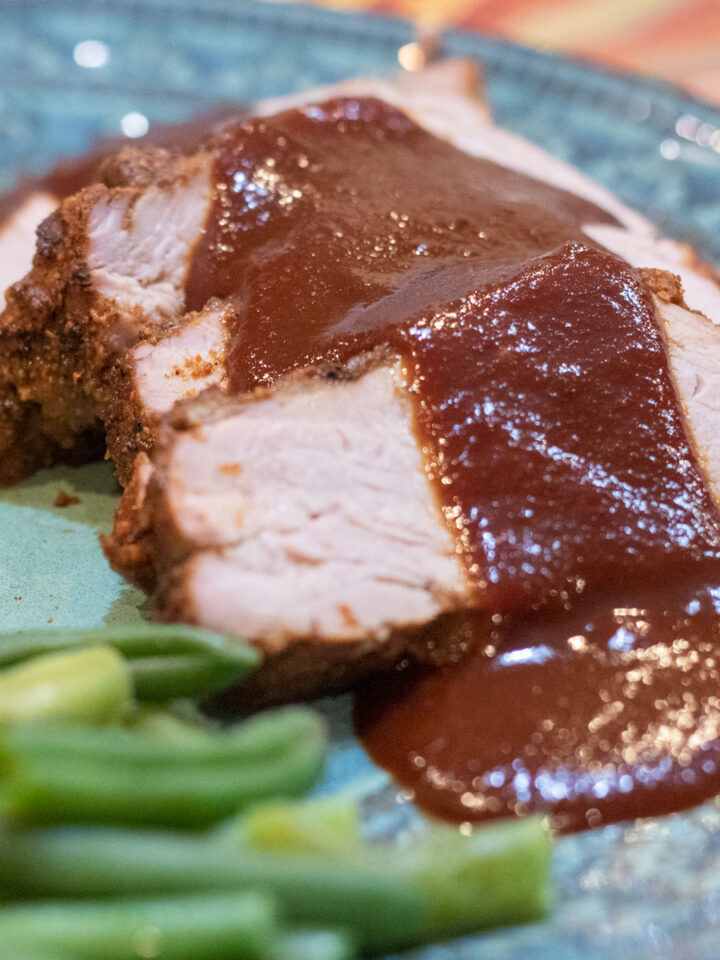 cranberry bbq sauce poured over port tenderloin with a side of green beans on a green dinner plate