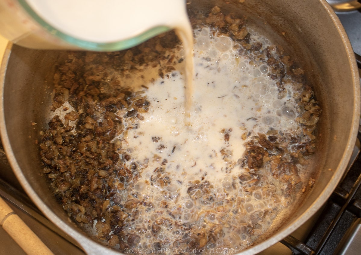 warmed milk added to veggie flour mixture in a frying pan