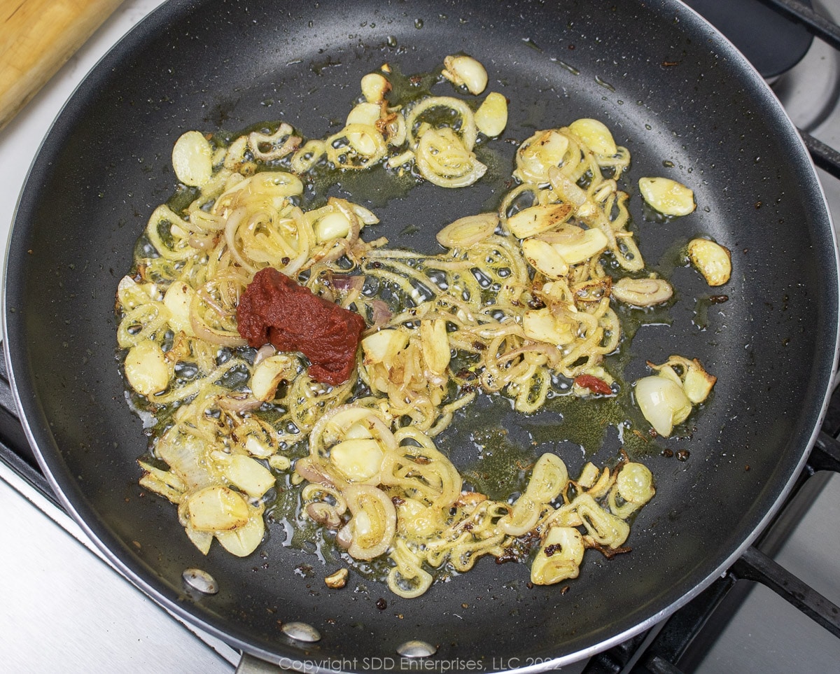 tomato paste added to shallots and garlic in a pan