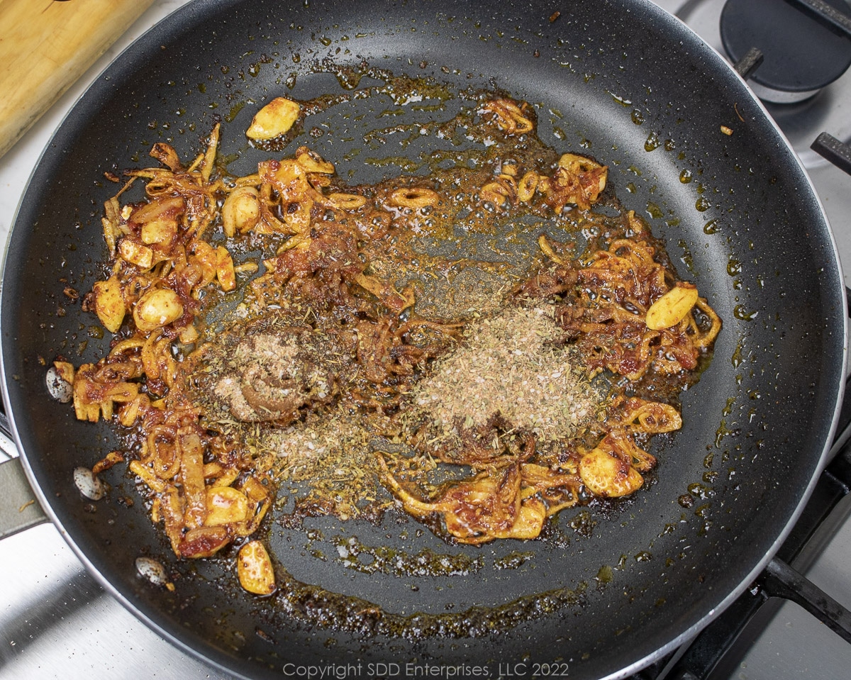 herbs and spices added to a saute pan with onions and tomato paste