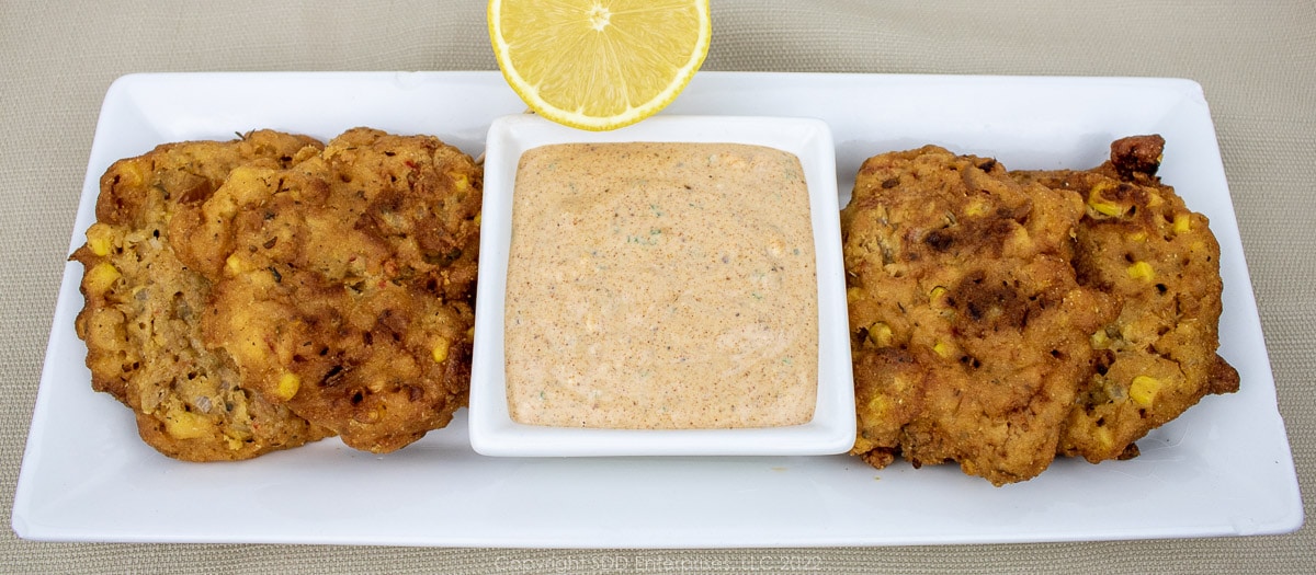 cajun dipping sauce with fritters and lemon half on white platter