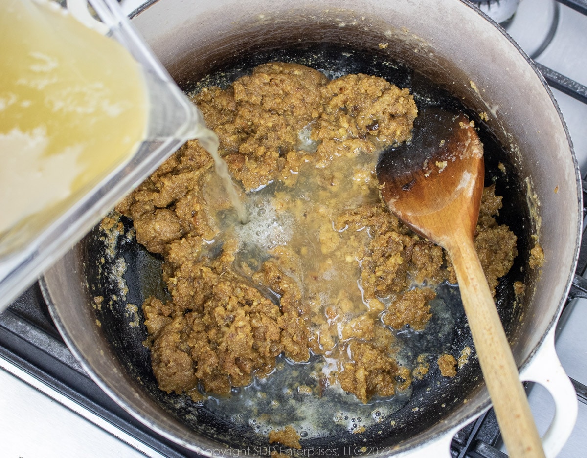 stock and oyster juice being slowly poured into sauteed vegetables in a Dutch oven