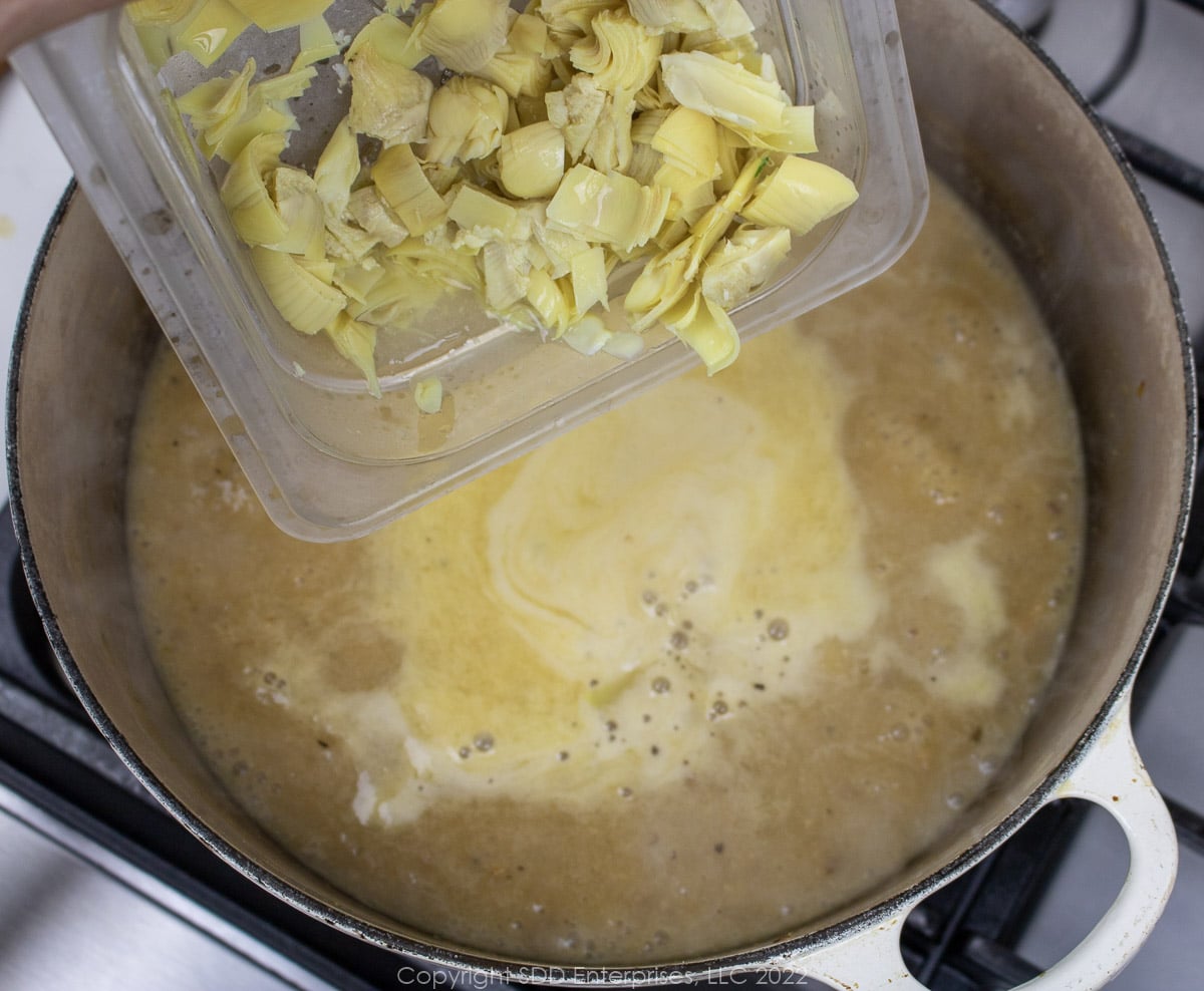 chopped artichoke hearts being added to a simmering liquid