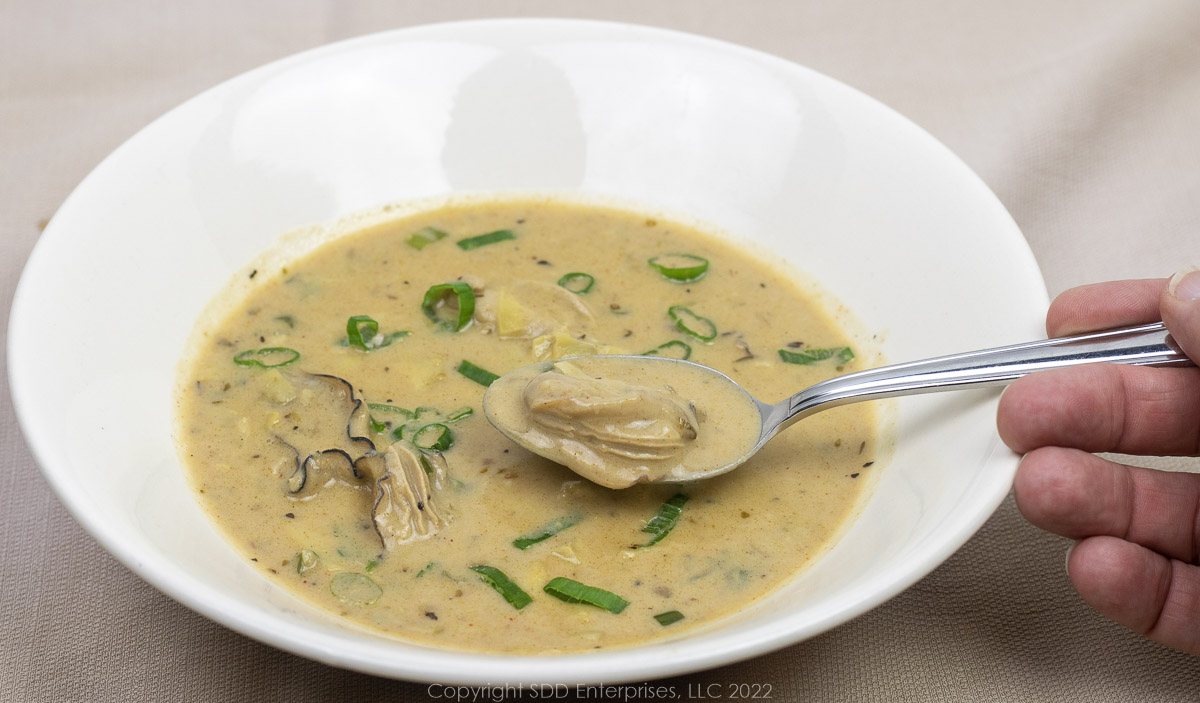 oyster artichoke bisque with garnish in a spoon and a white bowl