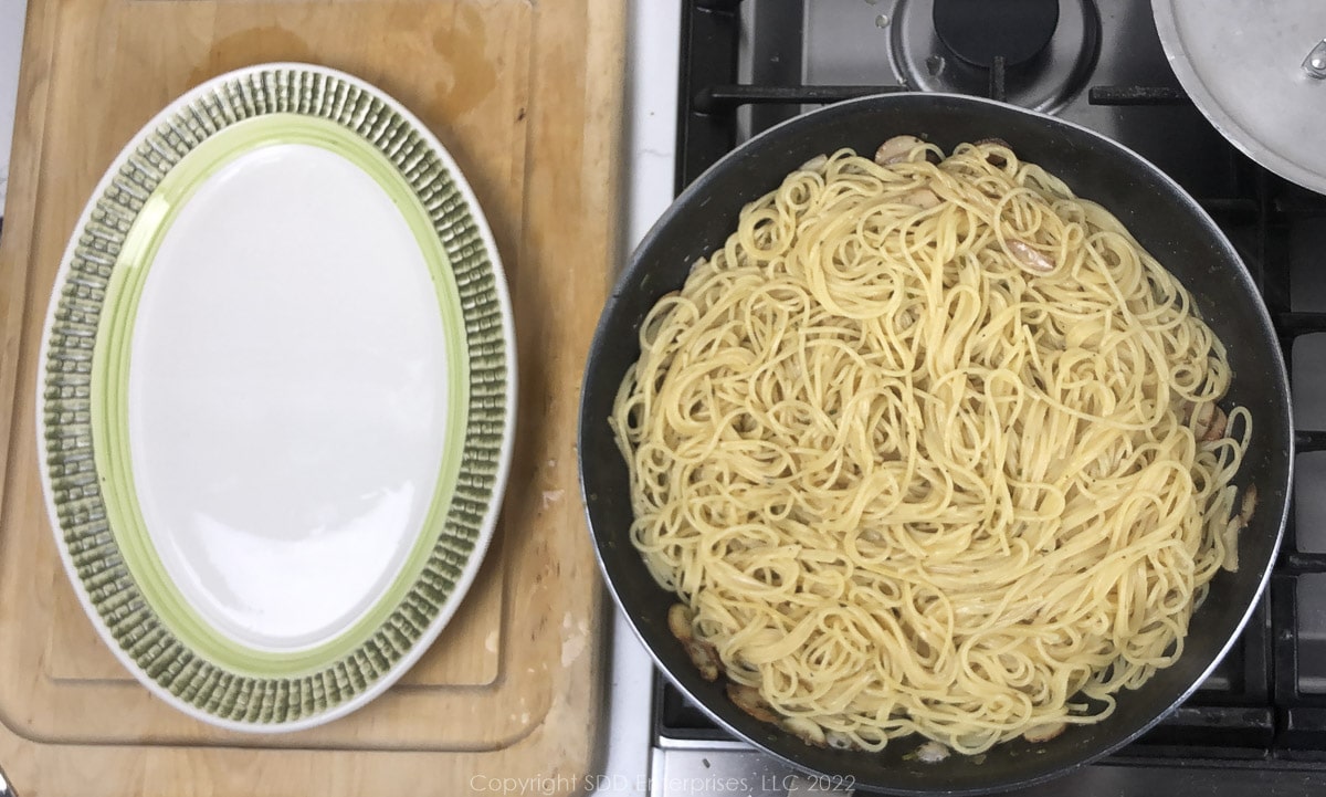 a pan of spghetti in butter sauce next to a green and white platter
