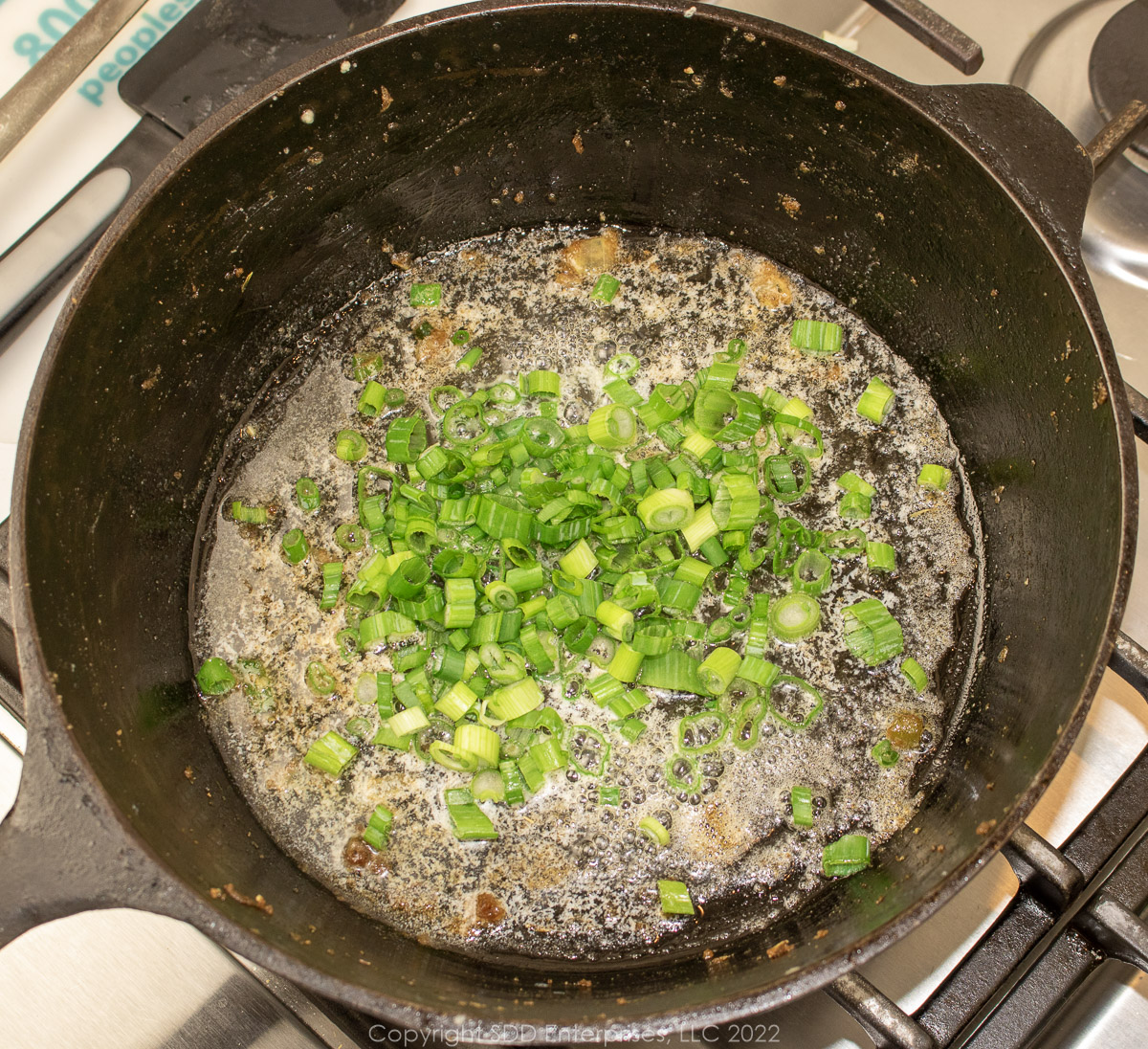 Sliced green onions added to butter in a cast iron Dutch oven.