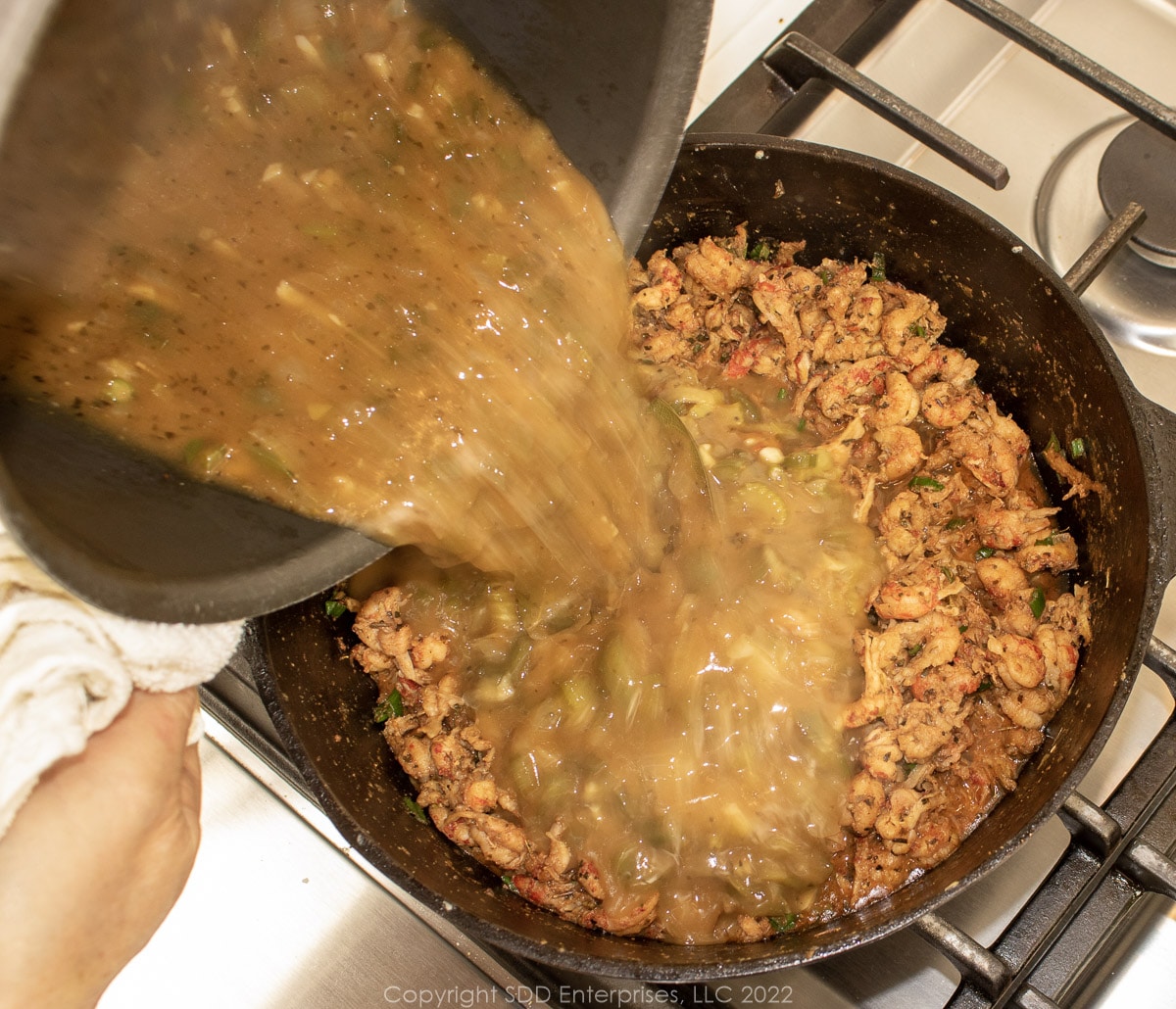 adding gravy to crawfish tails in a dutch oven
