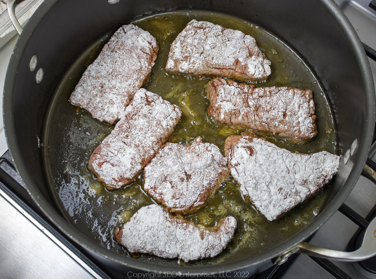 flour dusted round steak browning in a Dutch oven