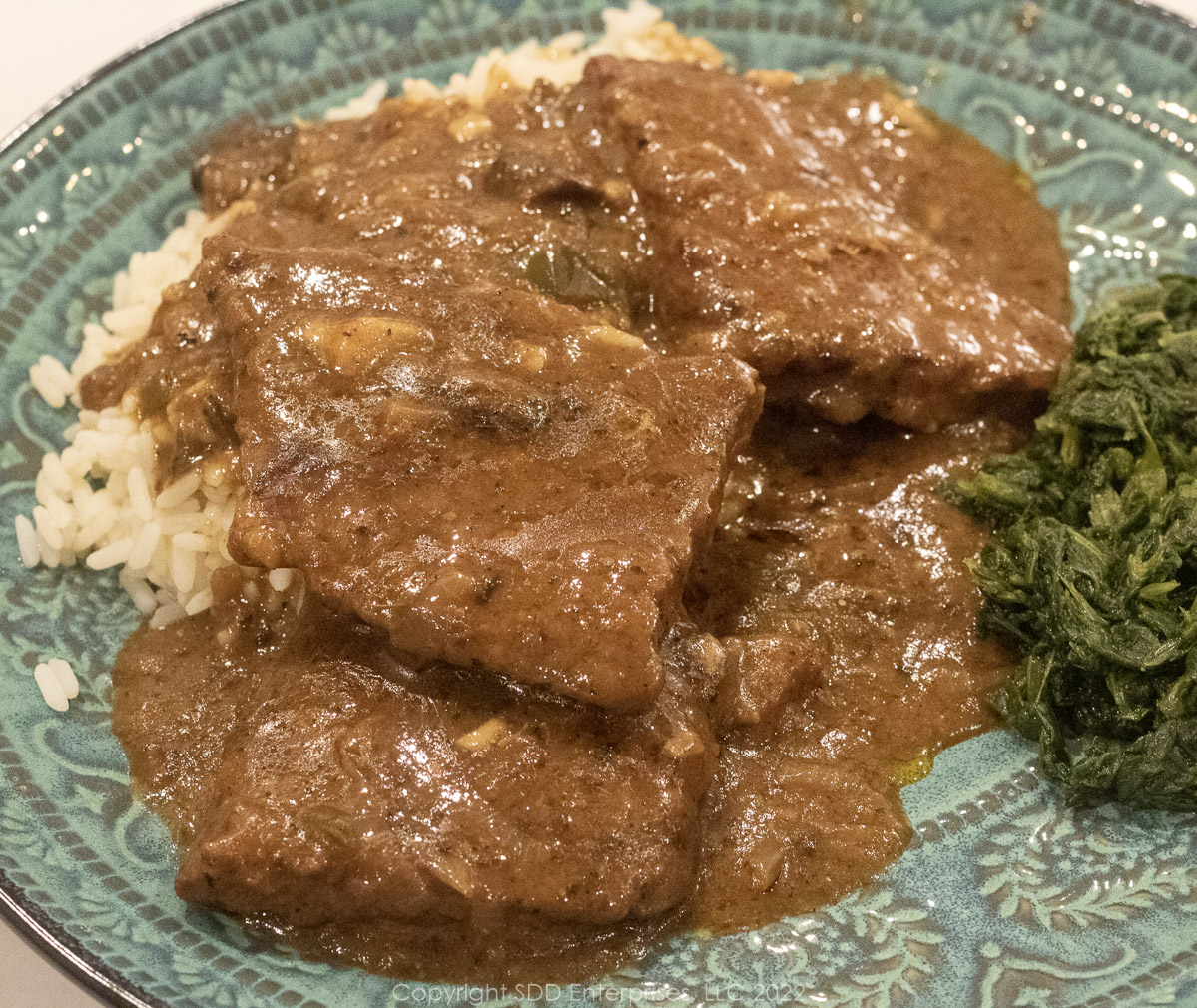 smothered round steak with rice and spinach on a blue green plate
