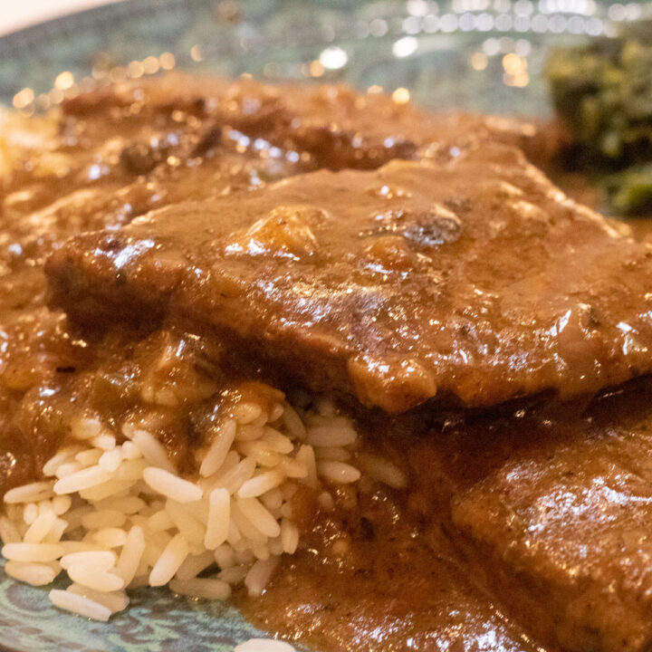 smothered round steak with rice and spinach on a green-blue plate