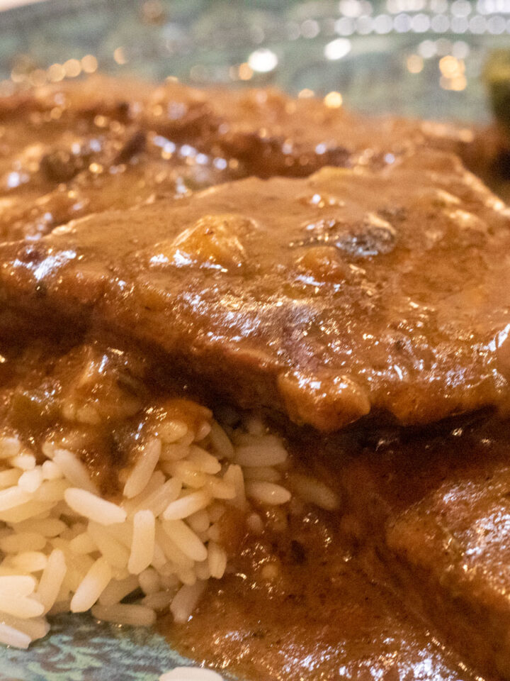 smothered round steak with rice and spinach on a green-blue plate