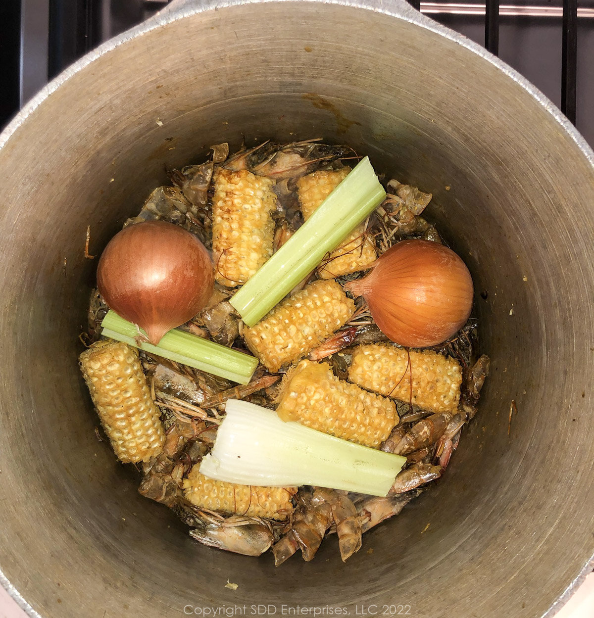 onins and celery added to corn cobs and shrimp shells in stockpot
